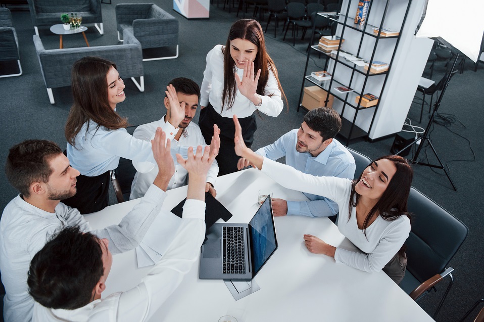 Giving high five to each other. Top view of office workers in classic wear sitting near the table using laptop and documents.