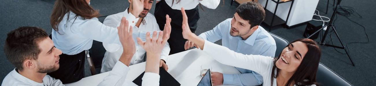 Giving high five to each other. Top view of office workers in classic wear sitting near the table using laptop and documents.